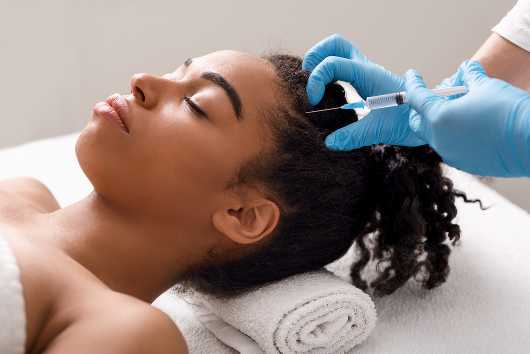 Medical professional in blue gloves administering a scalp injection for hair restoration therapy to a woman with natural curly hair lying on a treatment table.