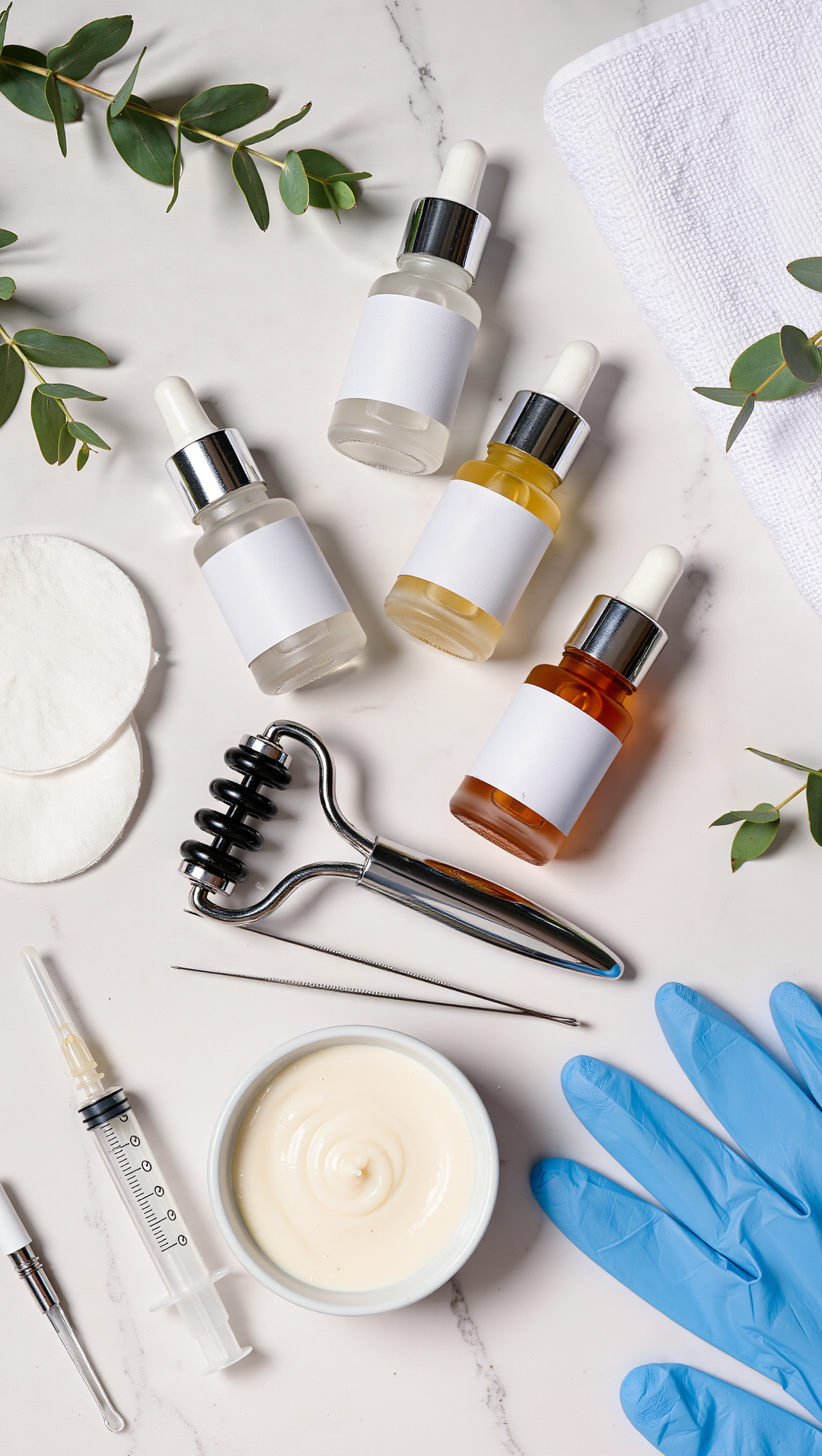 Cosmetic products including bottles, a candle, gloves, and tools on a light surface with greenery.